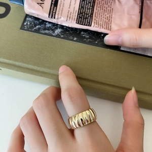 Gros plan d'une bague large dorée avec rayures verticales portée sur un doigt dans un décor chic