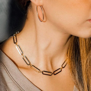 Golden paperclip chain necklace and hoop earrings jewelry set worn by a female model
