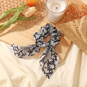 Close-up of leopard and snake print scrunchie with long ribbons on a wooden surface