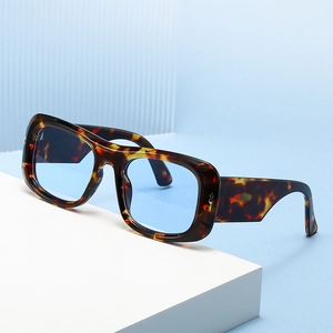 Fashionable tortoise shell wide frame sunglasses with light blue lenses on a geometric stand