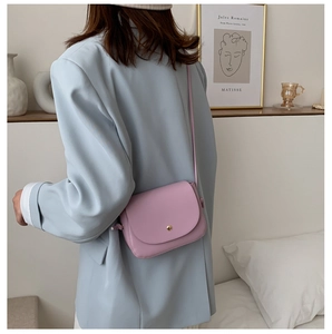 Detail of pink leather flap crossbody bag with gold hardware worn by a model in a blue suit