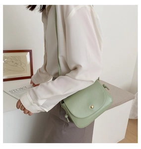 Close-up of a light green leather crossbody bag featuring a minimalist gold circular buckle