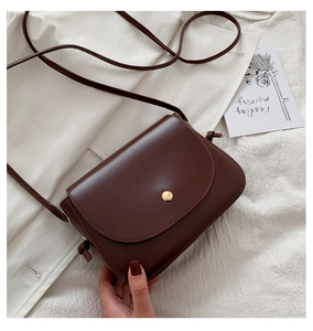 Close-up of vintage dark brown leather shoulder bag with gold hardware on white blazer