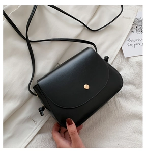 Detail of black faux leather crossbody bag featuring gold snap button and knotted strap