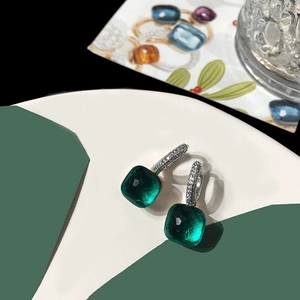 Detailed macro view of silver earrings featuring square emerald green stones and pave crystals
