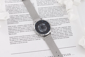 Close-up of silver mesh strap watch with black dial and blue markers on props
