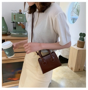 Dunkelbraune Mini-Handtasche mit runden Henkeln in einer Café-Umgebung