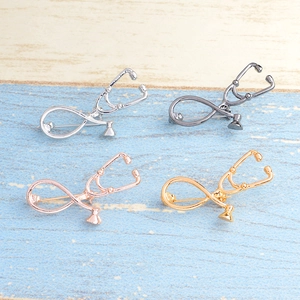 Flat lay of stethoscope brooches in silver, gun black, rose gold, and gold alloy finishes