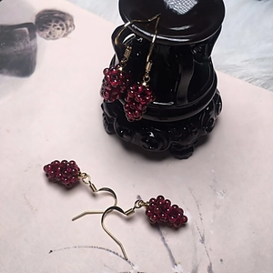 Macro detail of handmade garnet grape earrings with gold hooks on a black ceramic base
