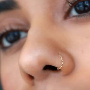 Minimalist golden twisted metal nose ring jewelry shown in a professional close-up shot