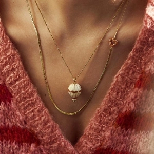 Gold hot air balloon and heart pendant necklace set with white enamel detail on a model
