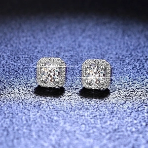 Macro shot of silver halo stud earrings with round moissanite center on textured blue background