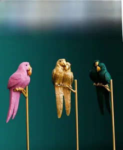 Detailed view of three resin parrot sculptures in pink, gold, and green with golden stands