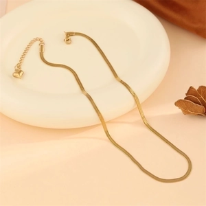 Minimalist gold flat snake chain necklace with heart charm in a warm aesthetic setting