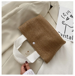 Close-up of woven straw handbag featuring white canvas handles and snap button closure