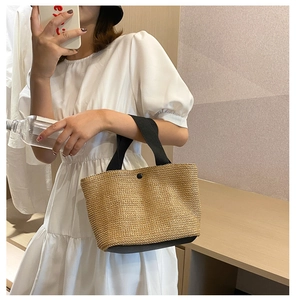 Detail of hand-woven straw tote with black handles, shown in a lifestyle mirror selfie