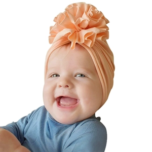 Détail d'un bonnet turban pour bébé en coton doux avec une grande fleur plissée rose abricot
