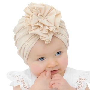 Gros plan détaillé d'un turban plissé beige pour bébé avec une grande fleur en tissu