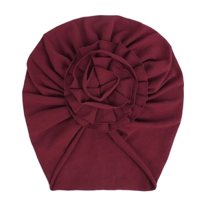 Détail d'un bonnet en coton tricoté rouge foncé pour bébé avec une grande fleur décorative