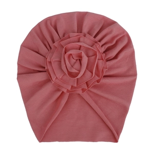 Détail d'un bonnet en maille rose pour bébé avec une grande fleur en tissu 3D multicouche
