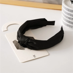 Close-up of a black satin knotted headband with a smooth silky texture on white props