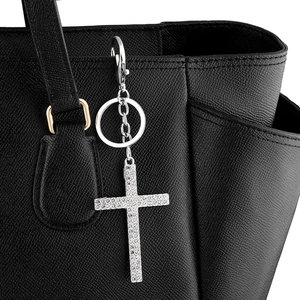 Detail of a sparkling silver cross keychain with rhinestones hanging on a black leather bag