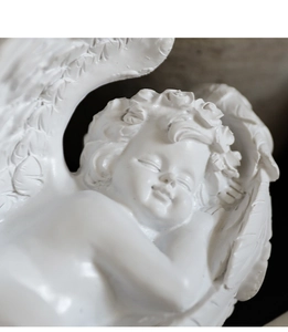 Détail d'une statue d'ange blanc endormi en résine montrant les plumes des ailes