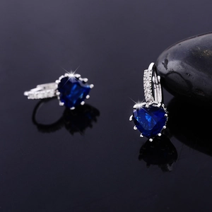 Macro detail of heart-shaped blue zircon earrings with silver setting on a black stone