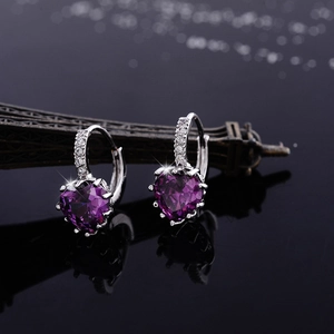 Detailed view of heart-shaped purple zircon earrings on a reflective surface