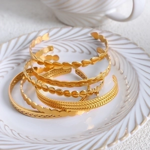 Set of five gold titanium steel open bangles with heart and braided texture details