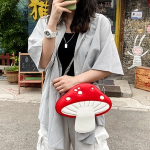 Detail of red mushroom crossbody bag with white dots and silver chain strap in outdoor setting