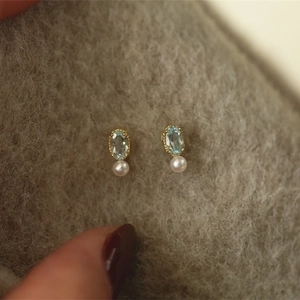 Macro detail of S925 silver gold-plated stud with blue topaz and round white pearl