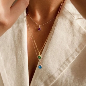 Close-up of triple layered gold necklaces with purple, green, and blue zircon pendants