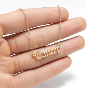 Hand holding gold Cancer zodiac pendant necklace with Gothic lettering on a fine chain