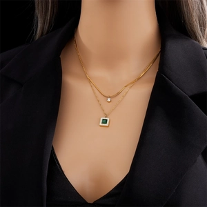 Double-layered gold chain necklace with square emerald green gemstone pendant worn by a model