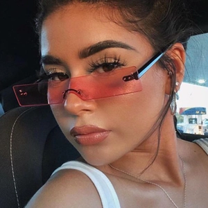 Close-up of red rimless rectangular sunglasses worn by a model in a trendy car setting
