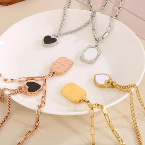 Detail of square shell and heart pendants on gold and silver layered necklaces in white dish