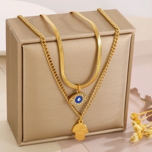 Close-up of layered gold Hamsa hand and blue Evil Eye pendants on luxury jewelry box