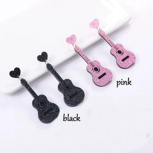 Detail view of pink and black glittery guitar earrings with heart-shaped studs on ceramic