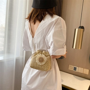 Detailed back view of a straw bucket bag with white daisy accents worn by a model