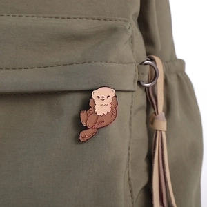 Cute cartoon sea otter enamel pin on a green nylon backpack, stylish ocean animal brooch