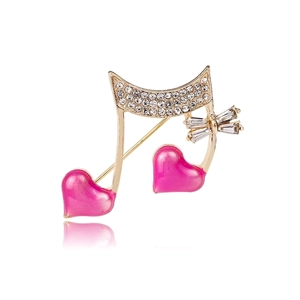 Detailed close-up of golden musical note brooch with pink hearts and sparkling crystals
