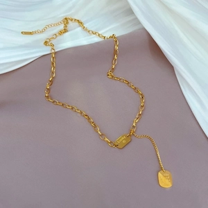 Macro detail of gold geometric tassel necklace with Lucky engraved pendant on chain