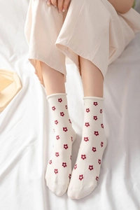 Close-up of beige crew socks with red floral pattern and stylish rolled edge cuffs