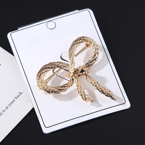 Detail of a handmade golden bow brooch with rope texture on a white display card