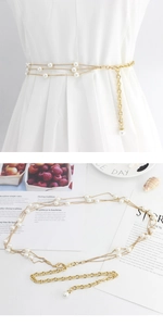 Detail of layered gold metal chain belt with white pearls on a white dress