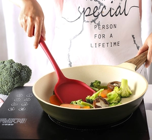 Detailed shot of dark red silicone spatula used in a non-stick pan with wood handle