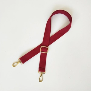 Détail d'une bandoulière en coton rouge avec crochets dorés et boucle réglable