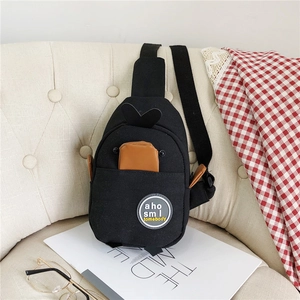 Detail of a black canvas crossbody bag with cartoon styling on a beige seat with props
