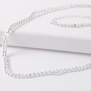 Silver layered necklace and bracelet set with delicate circular discs on white background